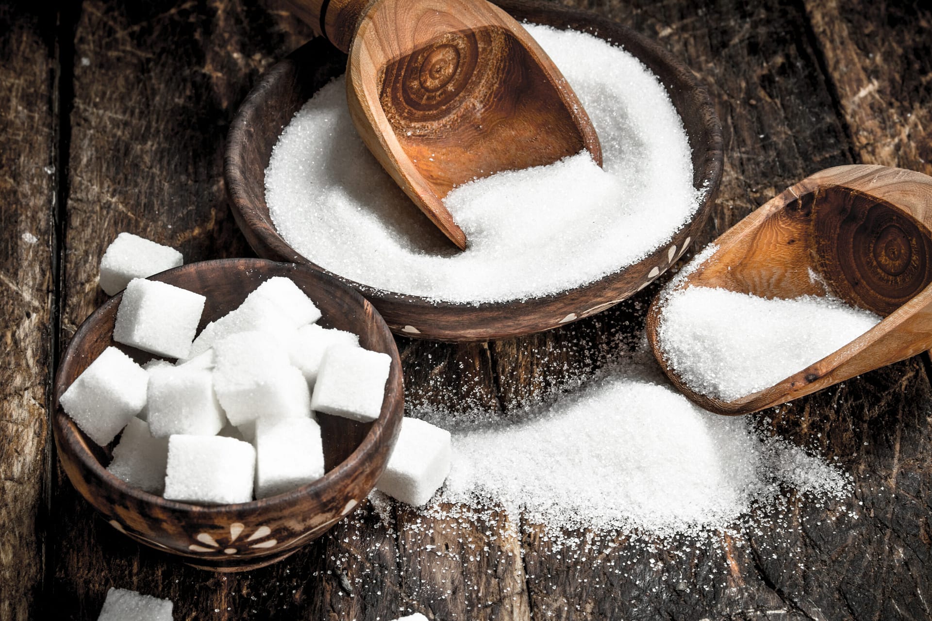 Sugar with a scoop in a bowl. On a wooden background.