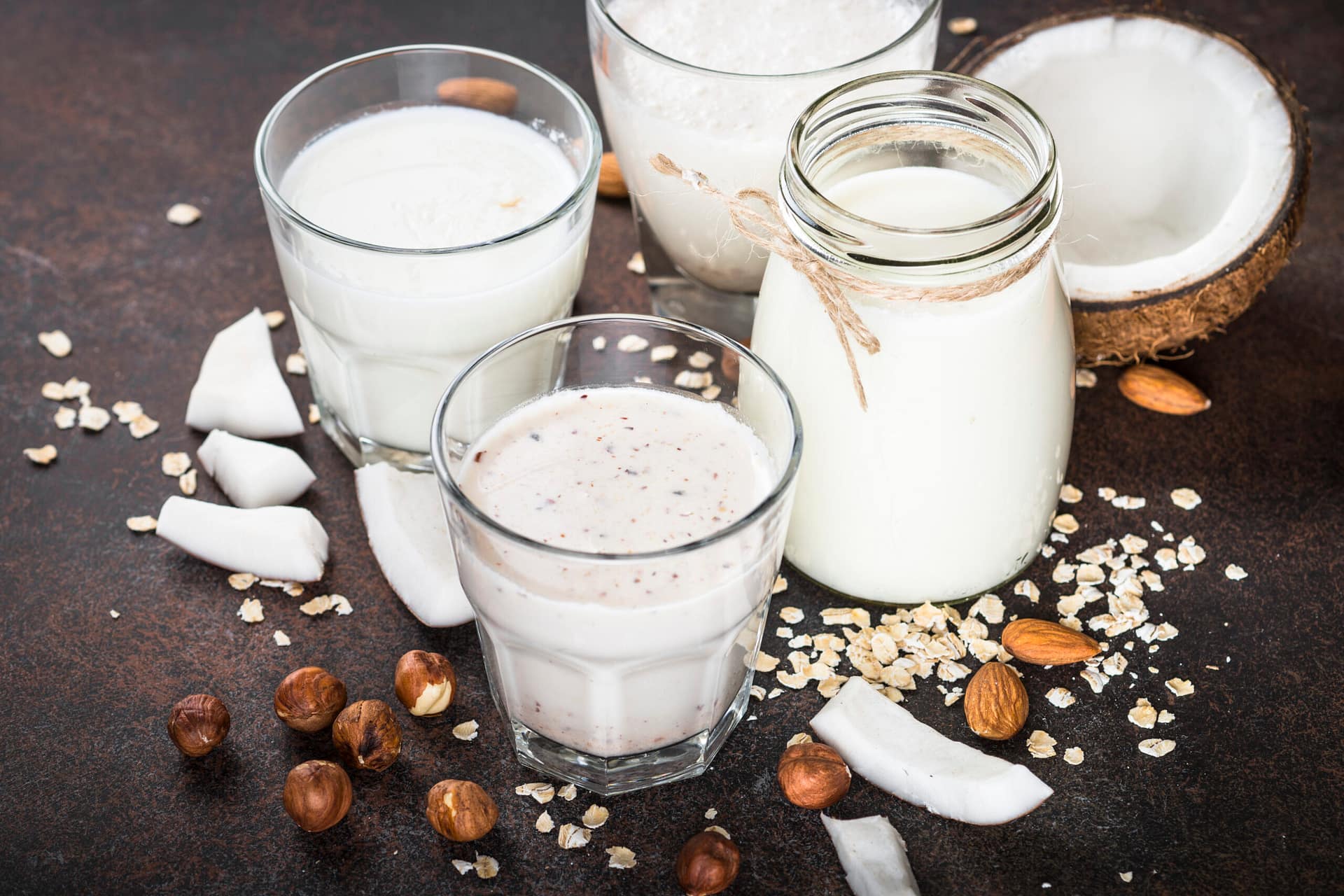 Vegan non dairy alternative milk. Coconut, almond, hazelnut, oat homemade milk on dark rusty table.